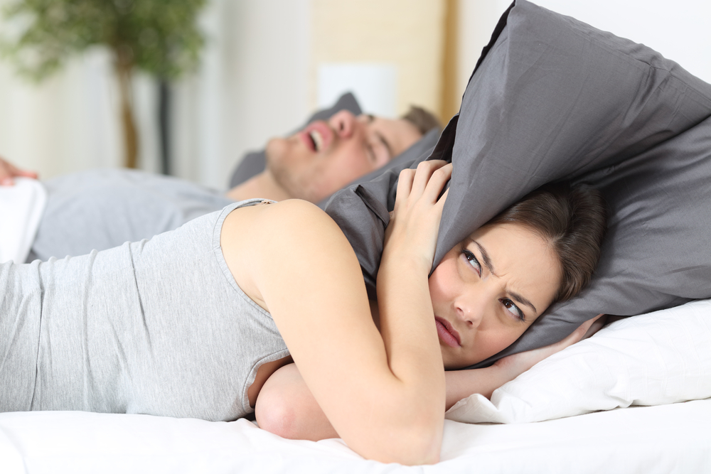 woman covering her ears with a pillow as her partner snores